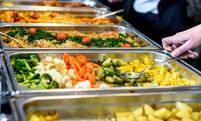 Eine Buffetlinie mit mehreren Personen, die sich Essen auf Teller servieren und miteinander sprechen.