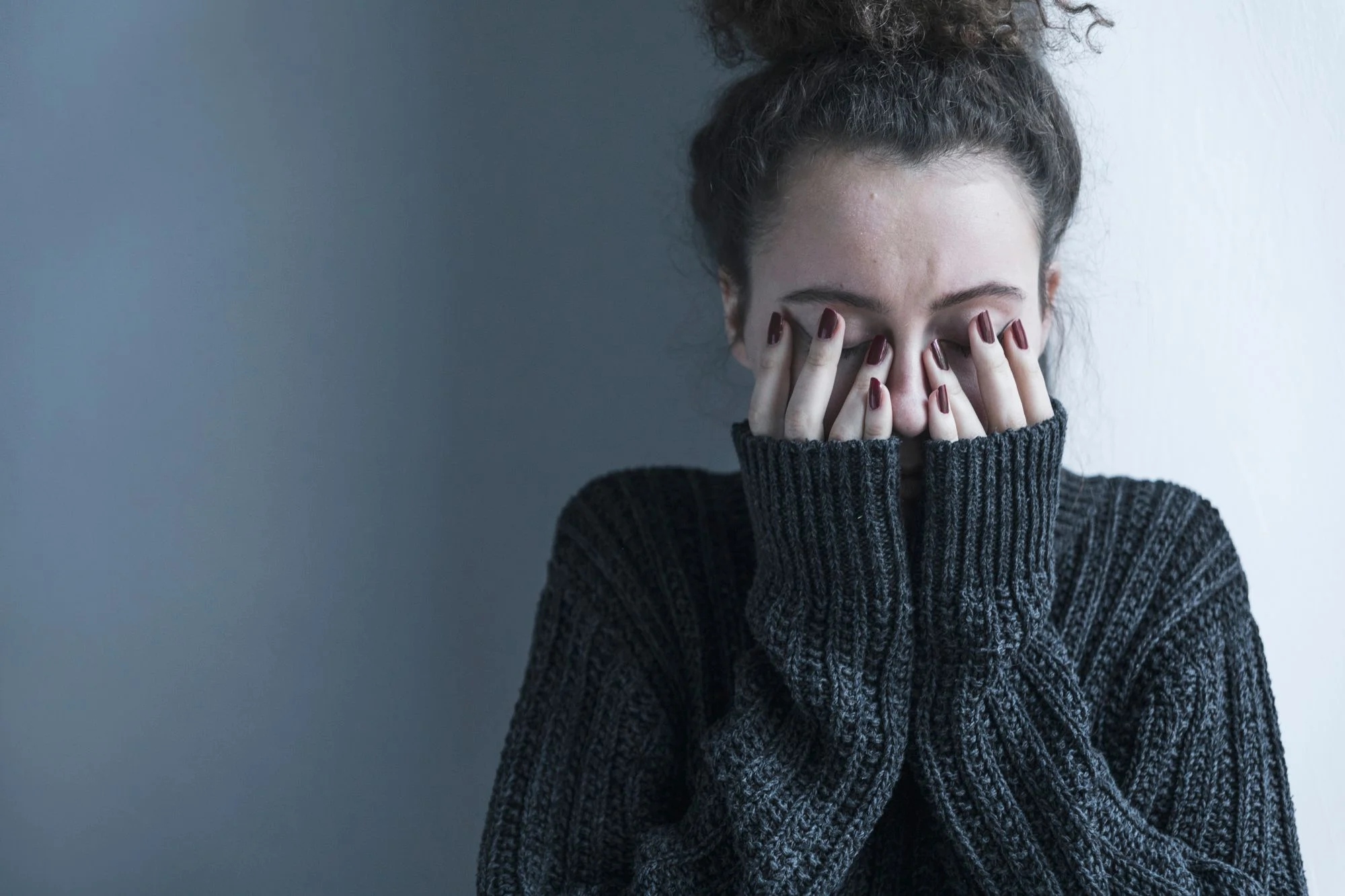 Nahaufnahme eines Teenagers mit Schizophrenie , der allein im Dunkeln sitzt. Sie bedeckt ihr Gesicht mit Händen. Psychische Probleme mit Depression und Bulimie.